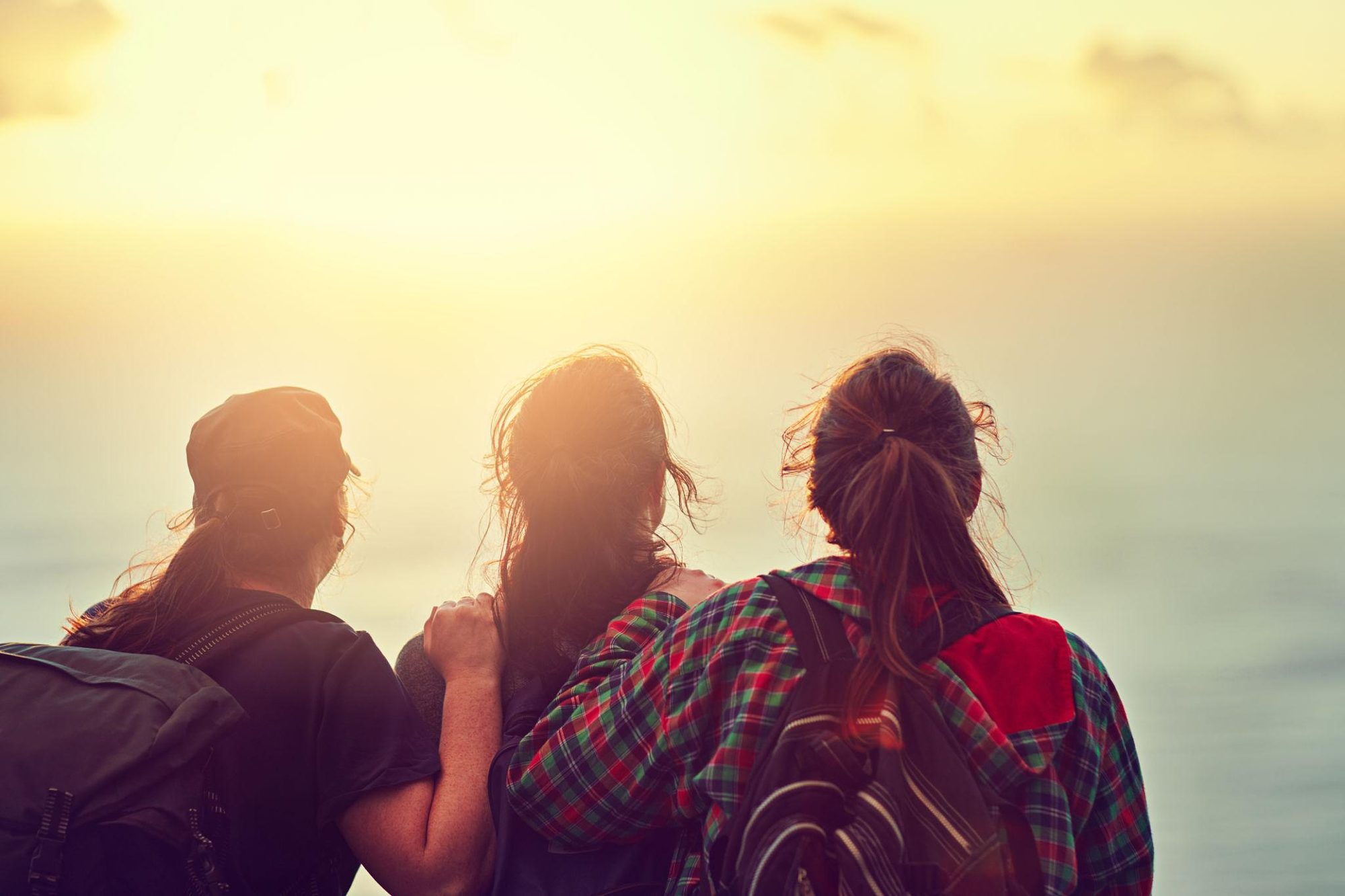 Three teenagers standing together looking out at a sunrise
